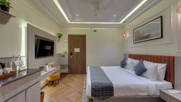 A hotel room with a bed, bedside table, TV, desk, chair, and a painting on the wall.