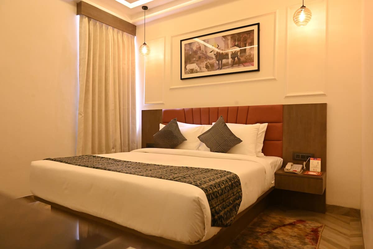 A neatly made bed with a patterned throw, a headboard with decorative pillows, a bedside table with a phone and a lamp, and a framed picture on the wall.