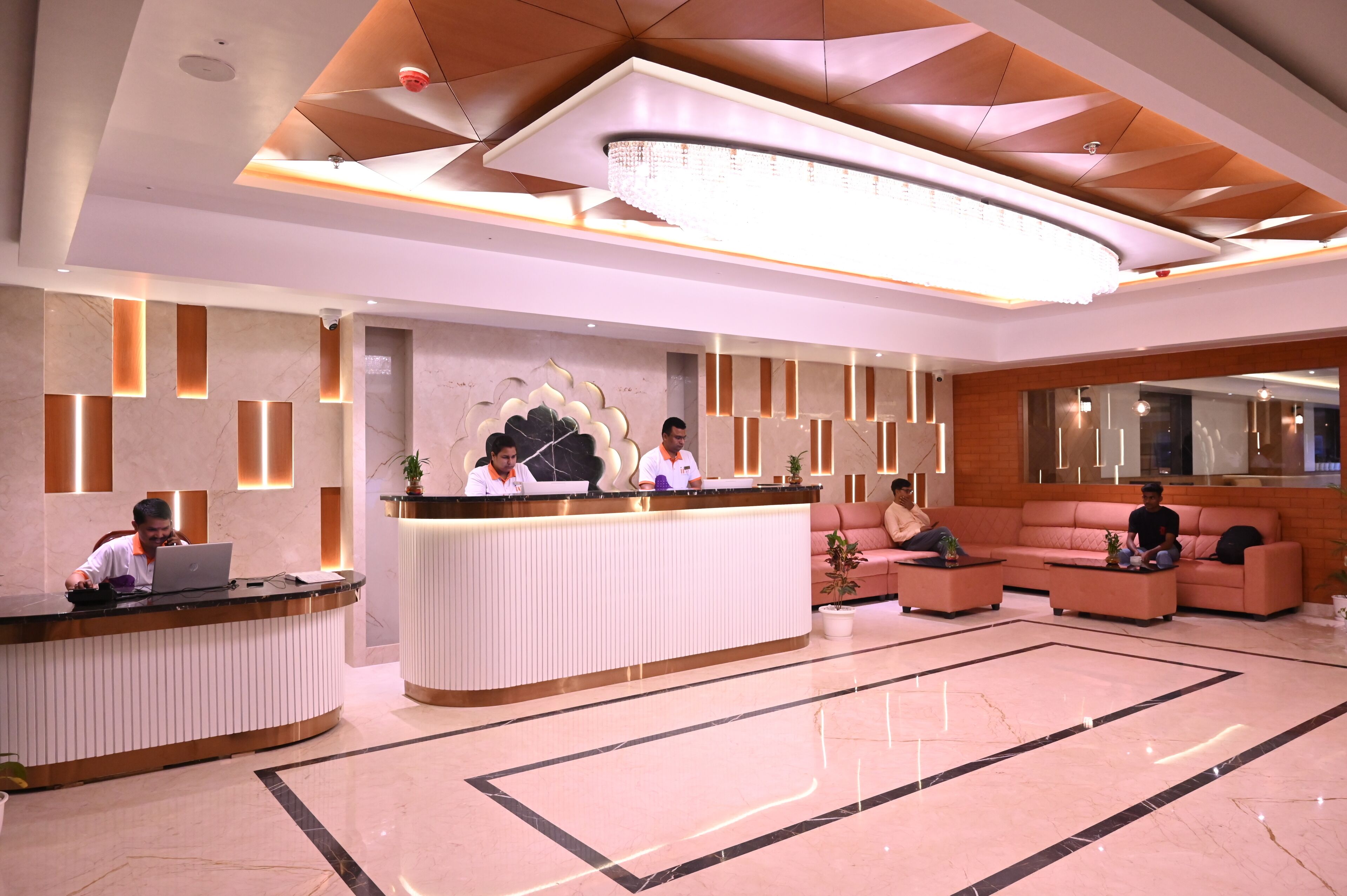 Un espace d’accueil d’hôtel au design moderne, comprenant un comptoir d’accueil, un coin salon et un lustre.