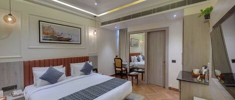 Quarto de hotel com uma cama grande, mesas de cabeceira, escrivaninha, cadeira, espelho e planta em vaso.