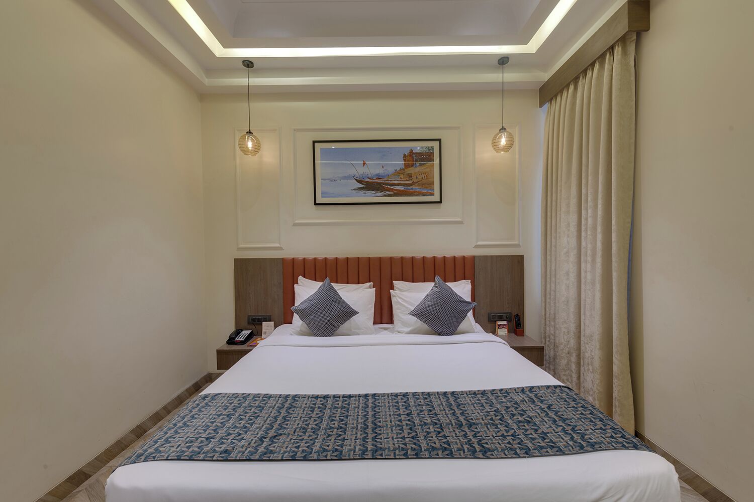 A hotel room with a large bed, two bedside tables, a painting on the wall, and a window with curtains.