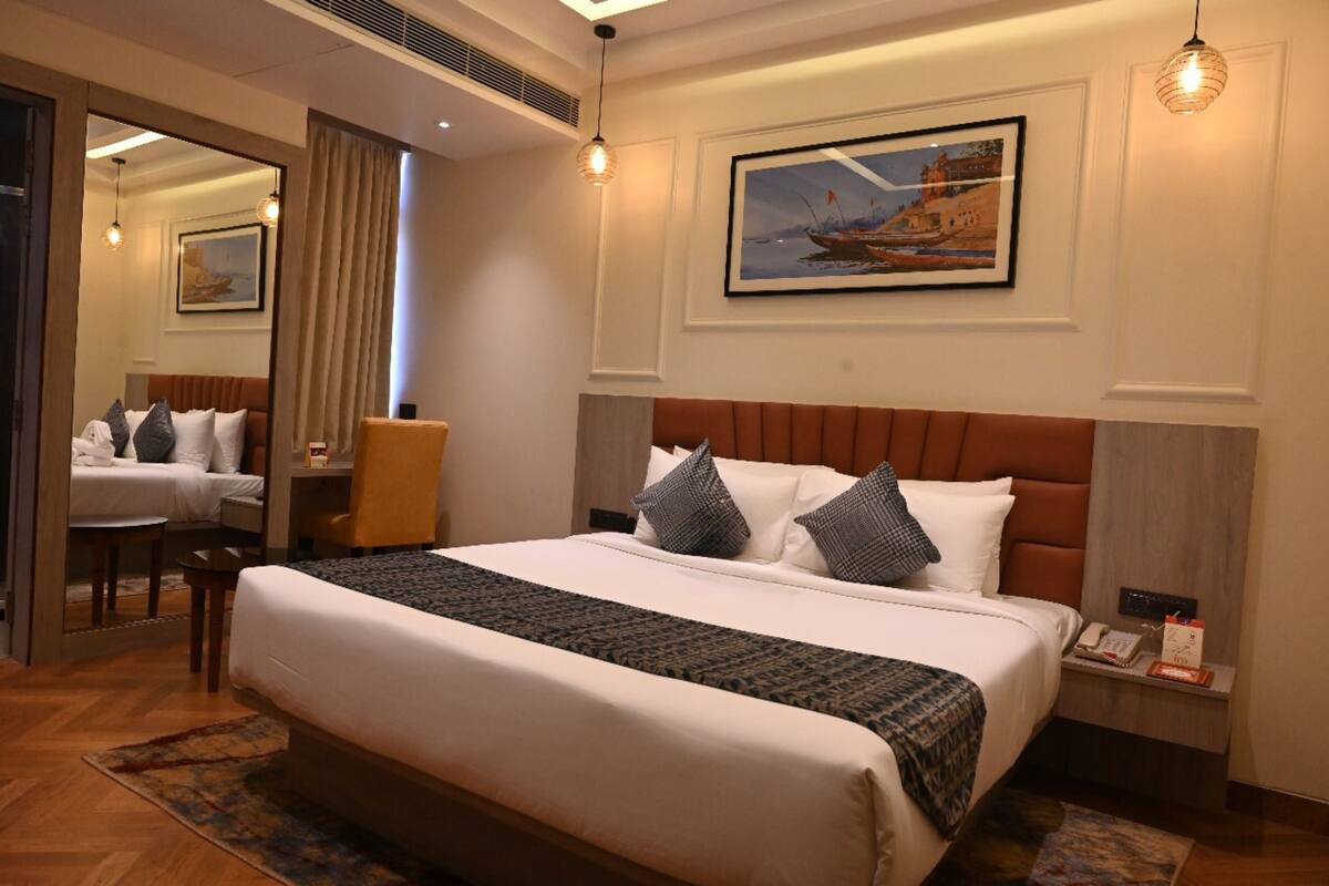 A hotel room with a large bed, a chair, a desk, a mirror, and a painting on the wall.