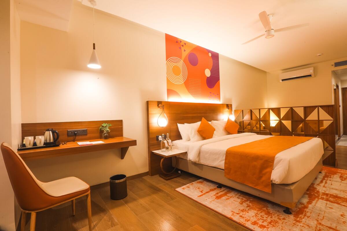 A hotel room with a bed, desk, chair, and a wall-mounted artwork.