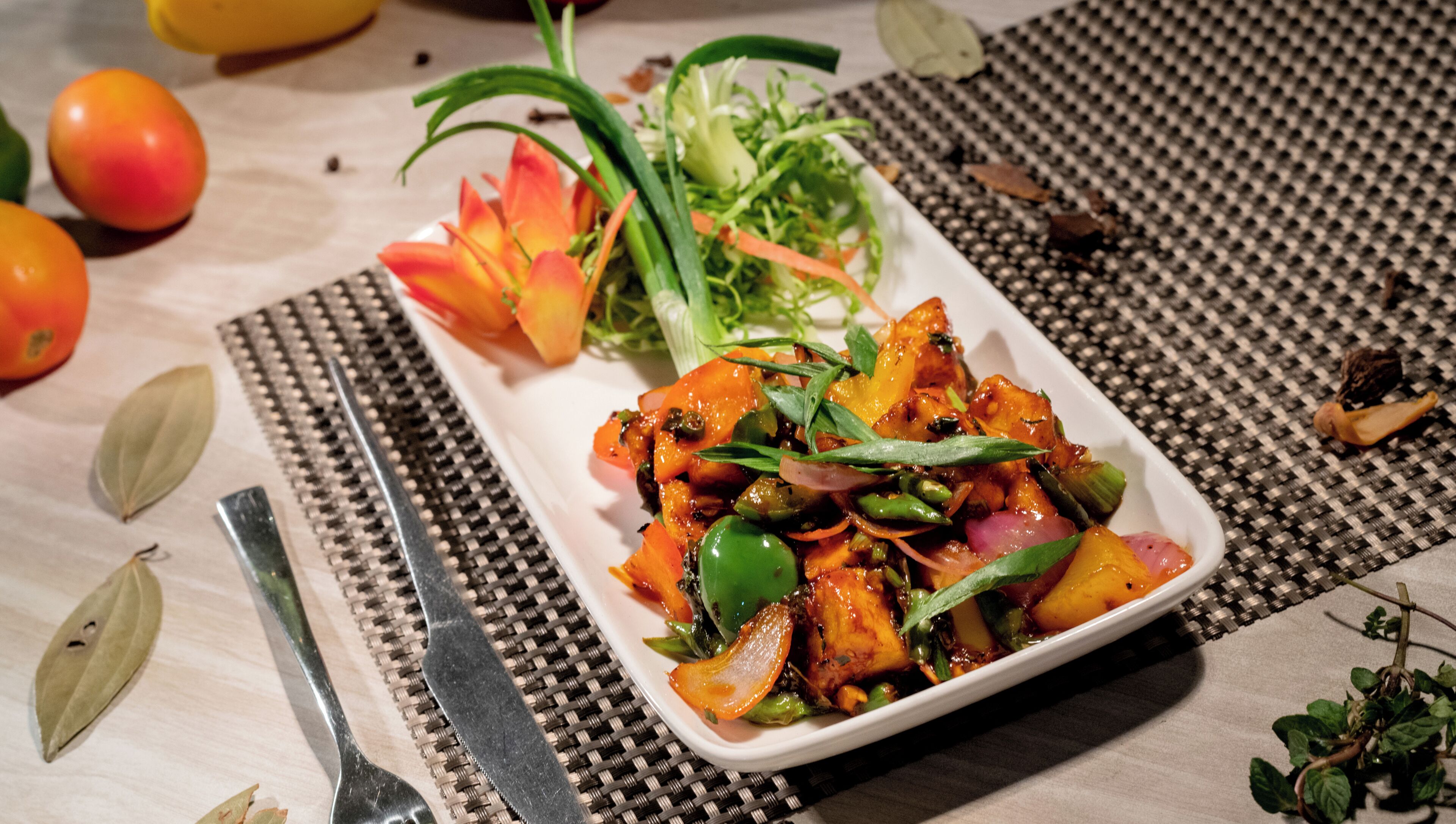 A rectangular white plate with a dish of mixed vegetables and herbs, a fork, and a woven placemat on a table.