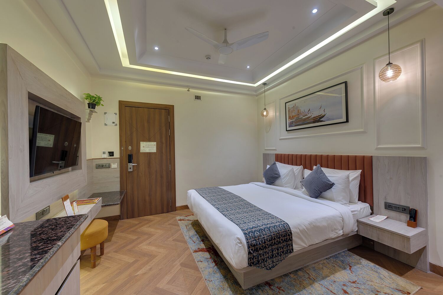 A modern hotel room with a bed, bedside table, TV, and a desk with a chair.