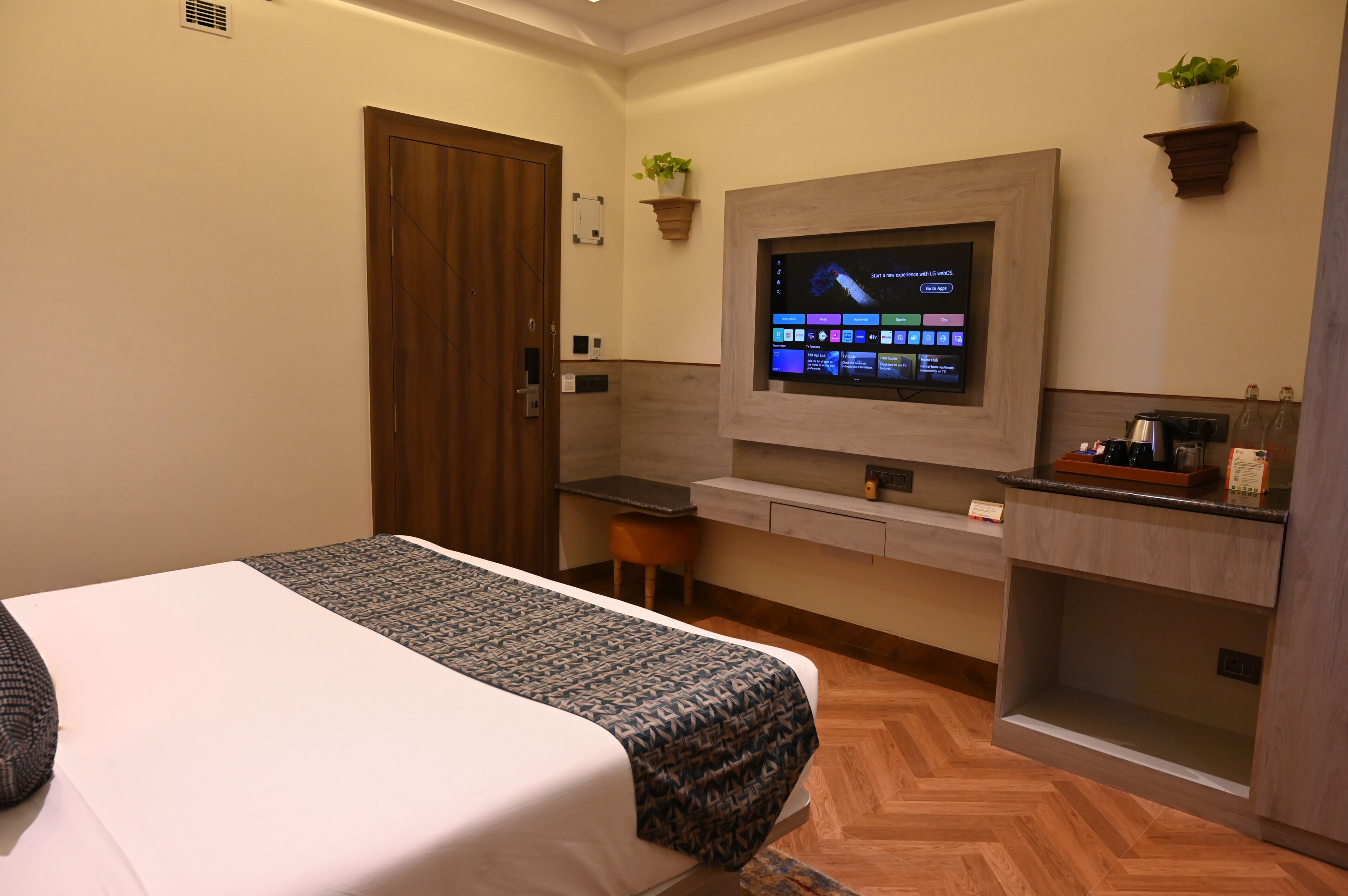 A hotel room with a bed, a desk, a TV, and a small kitchenette.