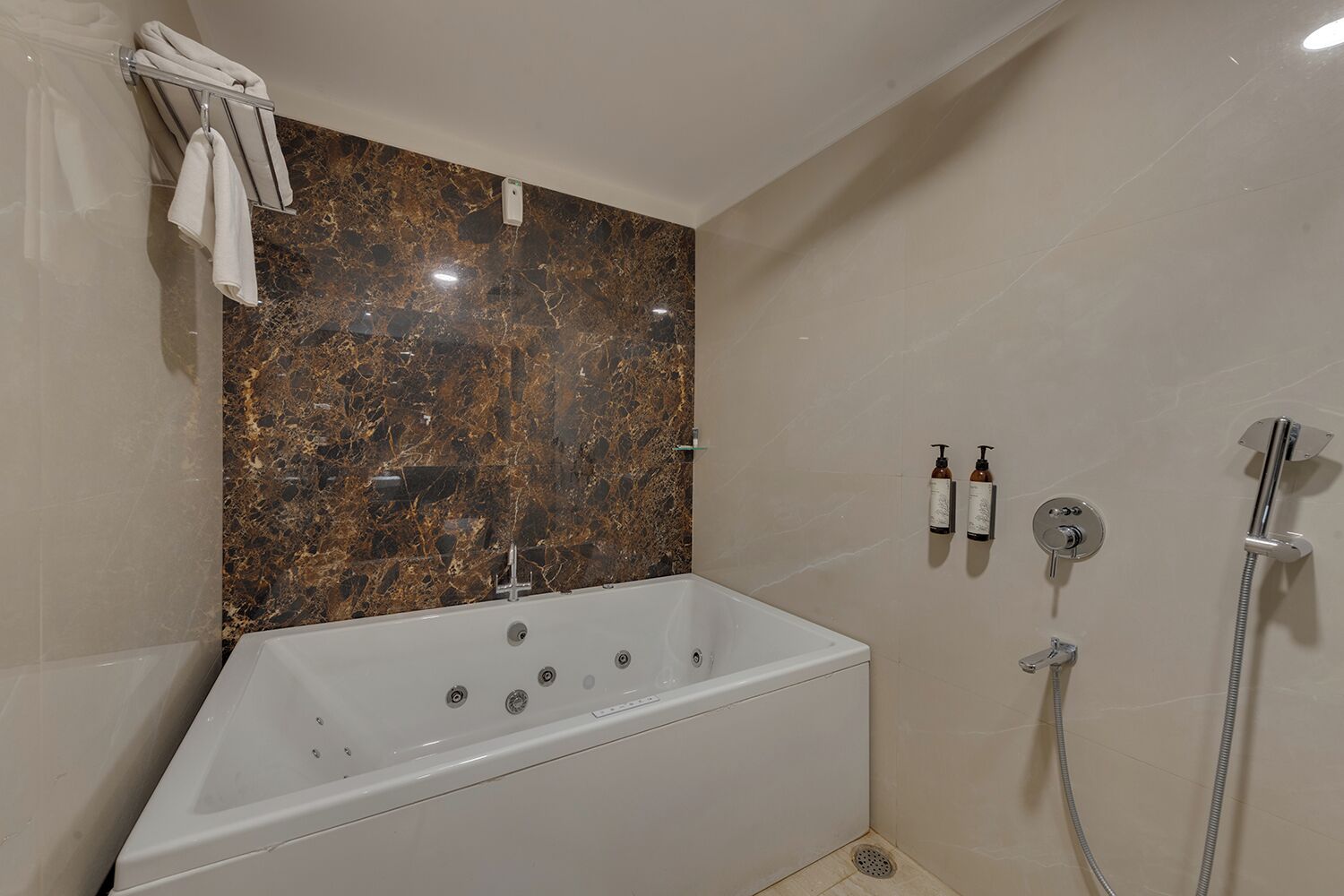 A bathroom with a marble wall, a bathtub, a shower, and two bottles of shampoo.