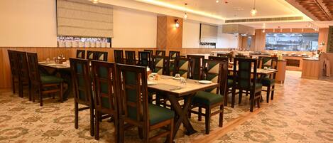 Un restaurant avec des tables et des chaises en bois, une moquette à motifs et des luminaires suspendus.