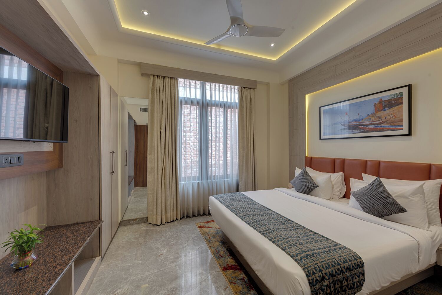 A modern hotel room with a large bed, a flat-screen TV, a ceiling fan, and a painting on the wall.