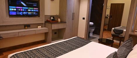 Een moderne hotelkamer met een groot bed, een flatscreen televisie aan de muur, een klein bureau en een badkamer door een open deur zichtbaar.
