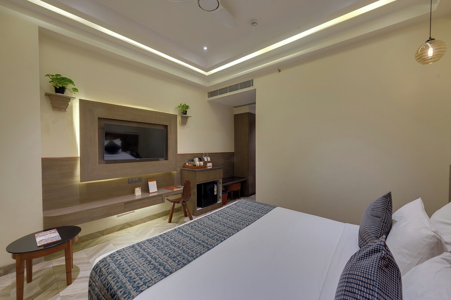 A modern hotel room with a large bed, a desk, a television, and a small seating area.