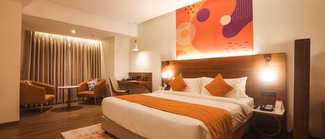 Habitación de hotel con una cama grande, un escritorio, dos sillas, un ventilador de techo y una pared con arte abstracto.