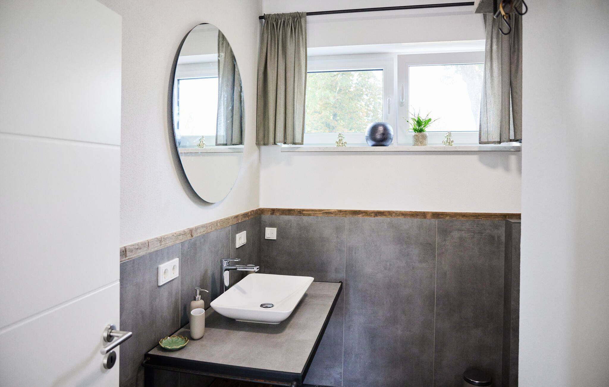 A bathroom with a white sink, a mirror, and a window with curtains.