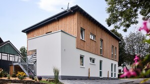 A modern two-story building with a wooden facade and white walls, featuring a staircase and a small garden area. - Beautiful apartment in Attendorn (Attendorn)