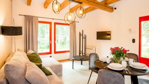 Een moderne woonkamer met een bank, een eettafel gedekt met borden, en een aan de muur bevestigde televisie.