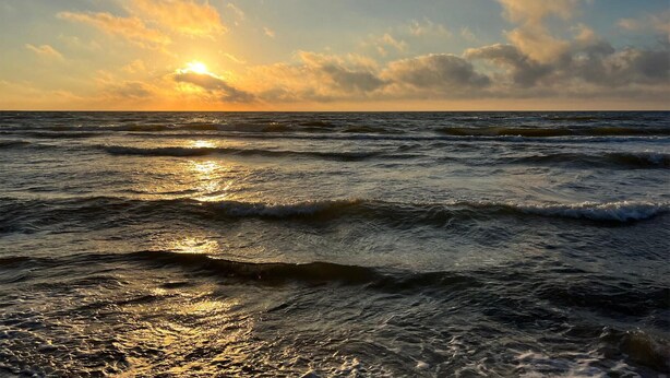 Een zonsondergang boven de oceaan met golven.