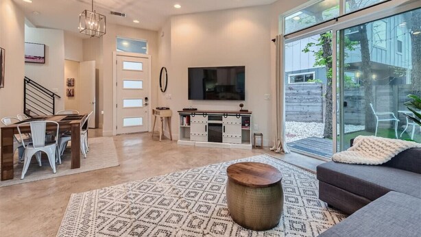 Sala de estar moderna com área de jantar, uma televisão grande e porta de vidro deslizante para um jardim.