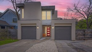 Uma casa moderna de dois andares com entrada de garagem, uma porta vermelha e uma entrada de automóveis que leva à garagem.
