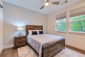 Une chambre à coucher avec un lit en bois, une table de chevet avec une lampe et une fenêtre donnant sur des arbres.