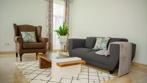 A living room with a brown leather armchair, a grey sofa, a wooden coffee table, and a patterned rug. - DivineHeights Apartment Lilongwe Area 43 (Lilongwe)