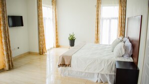 A bedroom with a bed, a TV mounted on the wall, a potted plant, and curtains. - DivineHeights Apartment Lilongwe Area 43 (Lilongwe)