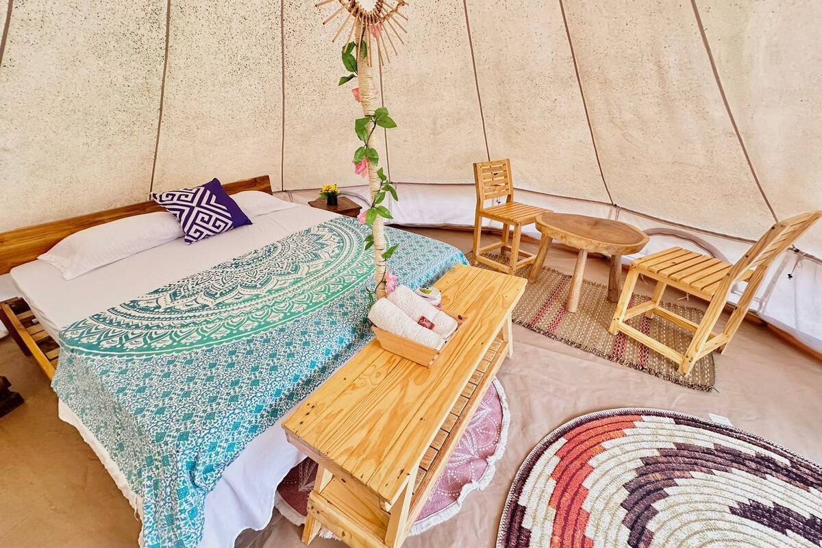 Eine Zelthütte mit Bett, kleinem Tisch, zwei Stühlen und einer dekorativen Hängung.
