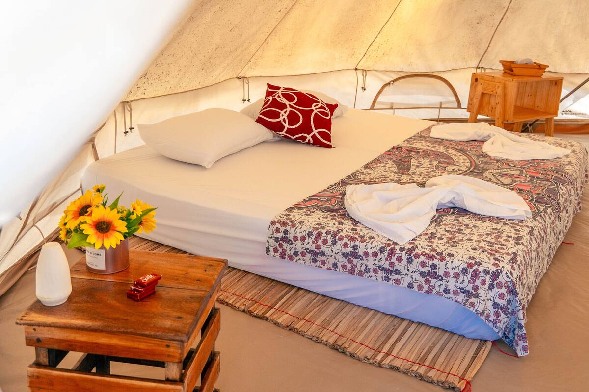Eine gemütliche Zeltoase mit Bett, Kissen, einem kleinen Holztisch mit Blumenvase und einer Matte.