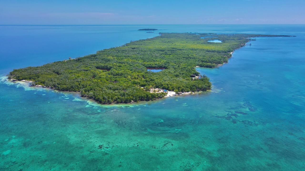 Vista aérea de una isla tropical con aguas turquesas cristalinas, vegetación verde exuberante y algunos edificios pequeños.
