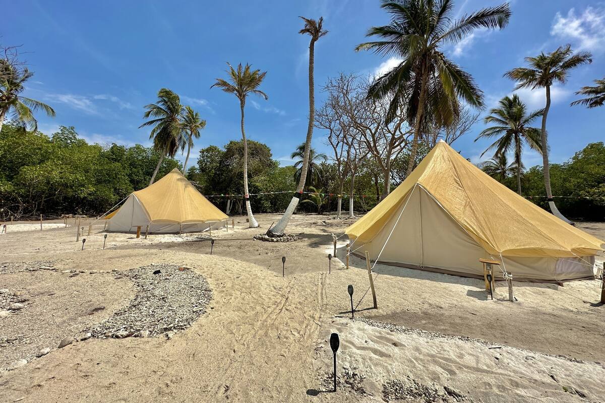 Zwei große Zelte an einem sandigen Strand, im Hintergrund Palmen.