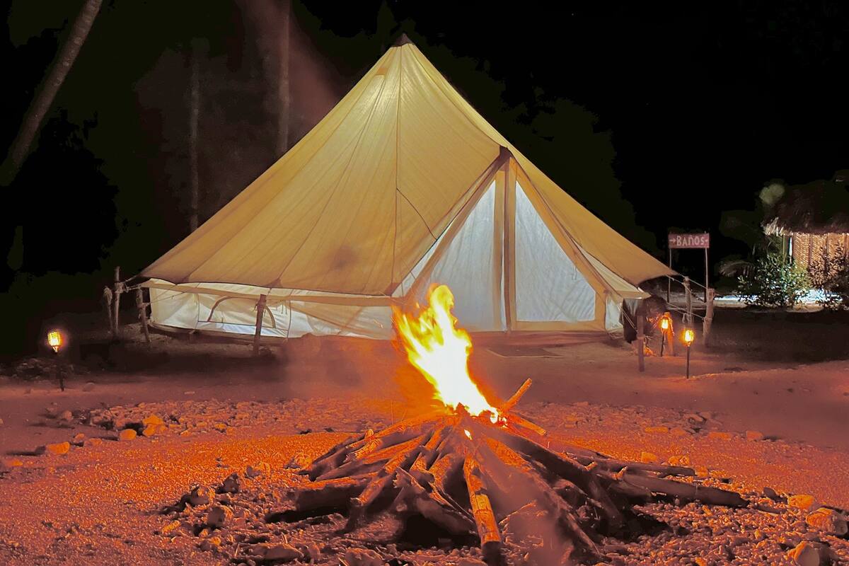 Ein Zelt mit Feuer davor, umgeben von Steinen und Bäumen.