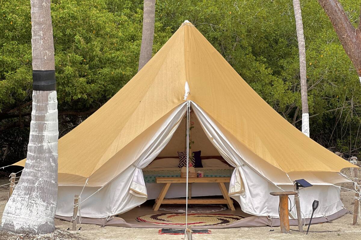 Ein großes, beige gefärbtes, pyramidenförmiges Zelt mit Liegefläche in der Mitte und einem kleinen Tisch.