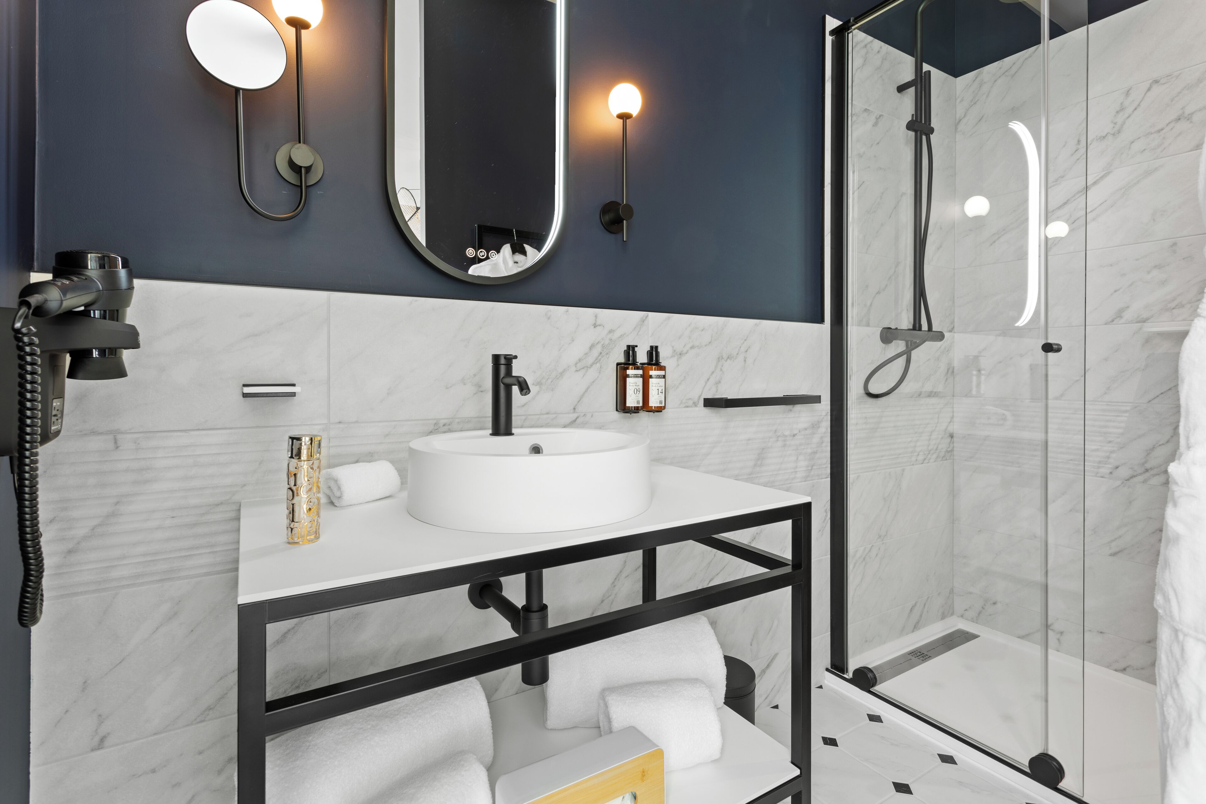 Un baño moderno con un lavabo blanco, grifo negro y una ducha con mampara de vidrio.