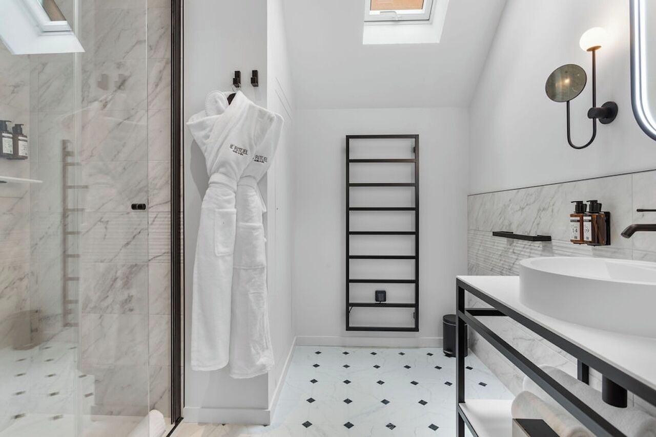 A modern bathroom with a skylight, a white bathtub, a black towel rack, and a marble floor.