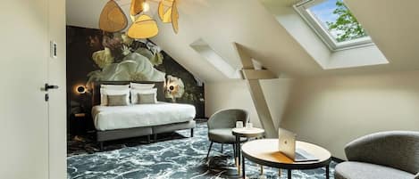 Ein modernes Hotelzimmer mit einem Bett, einem Schreibtisch mit einem Laptop, einem Sessel und einem Dachfenster.