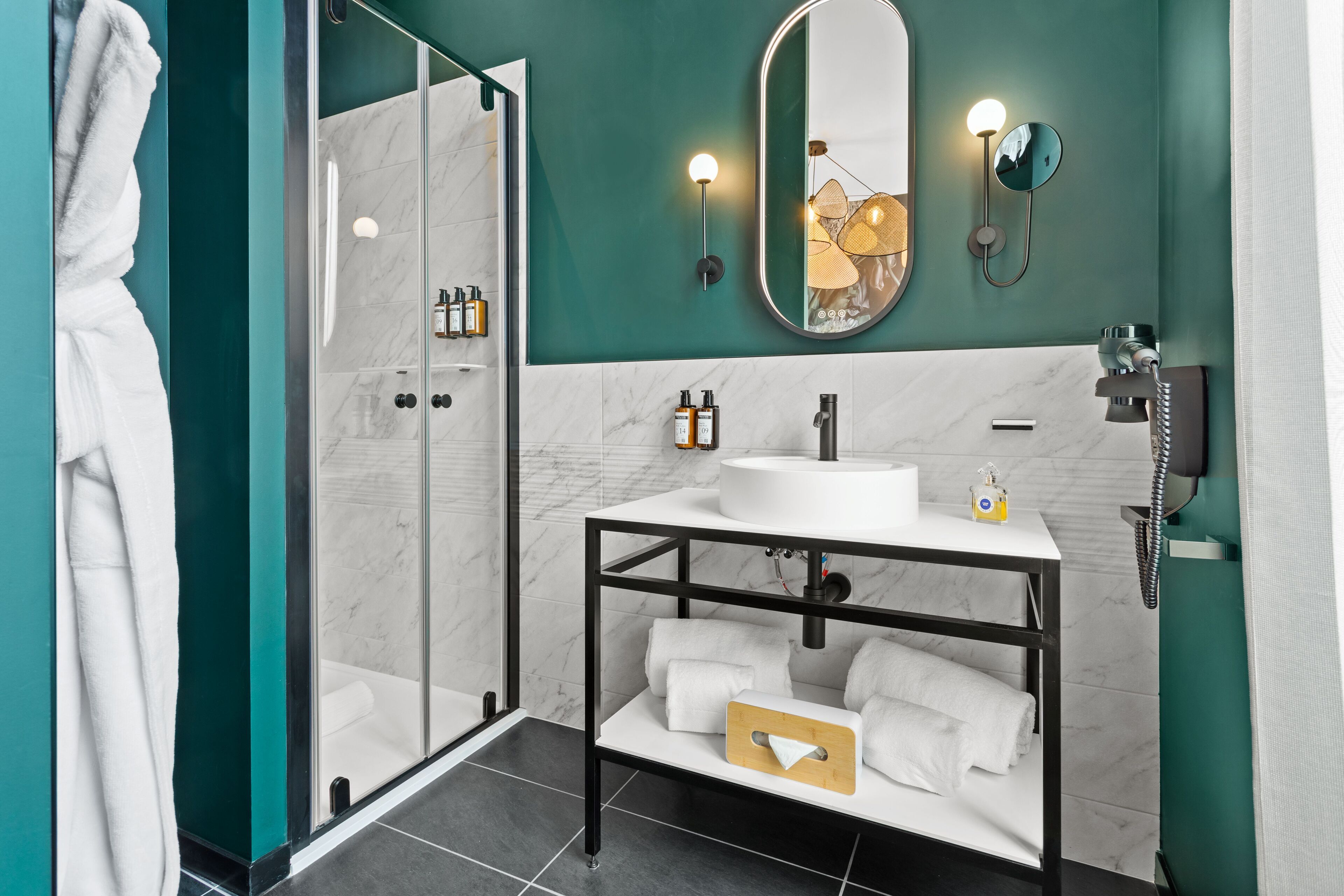 A modern bathroom with a glass-enclosed shower, a white sink with a mirror above it, and a towel rack with white towels.