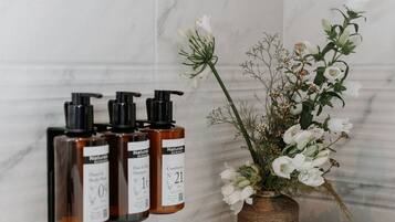 A bathroom with marble walls, a white bathtub, and three brown bottles labeled "Natural" on a shelf.