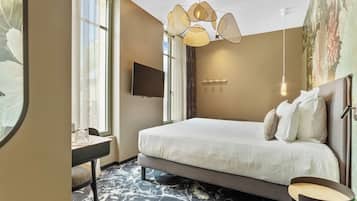 A hotel room with a bed, a desk, a television, a chandelier, and a large window.