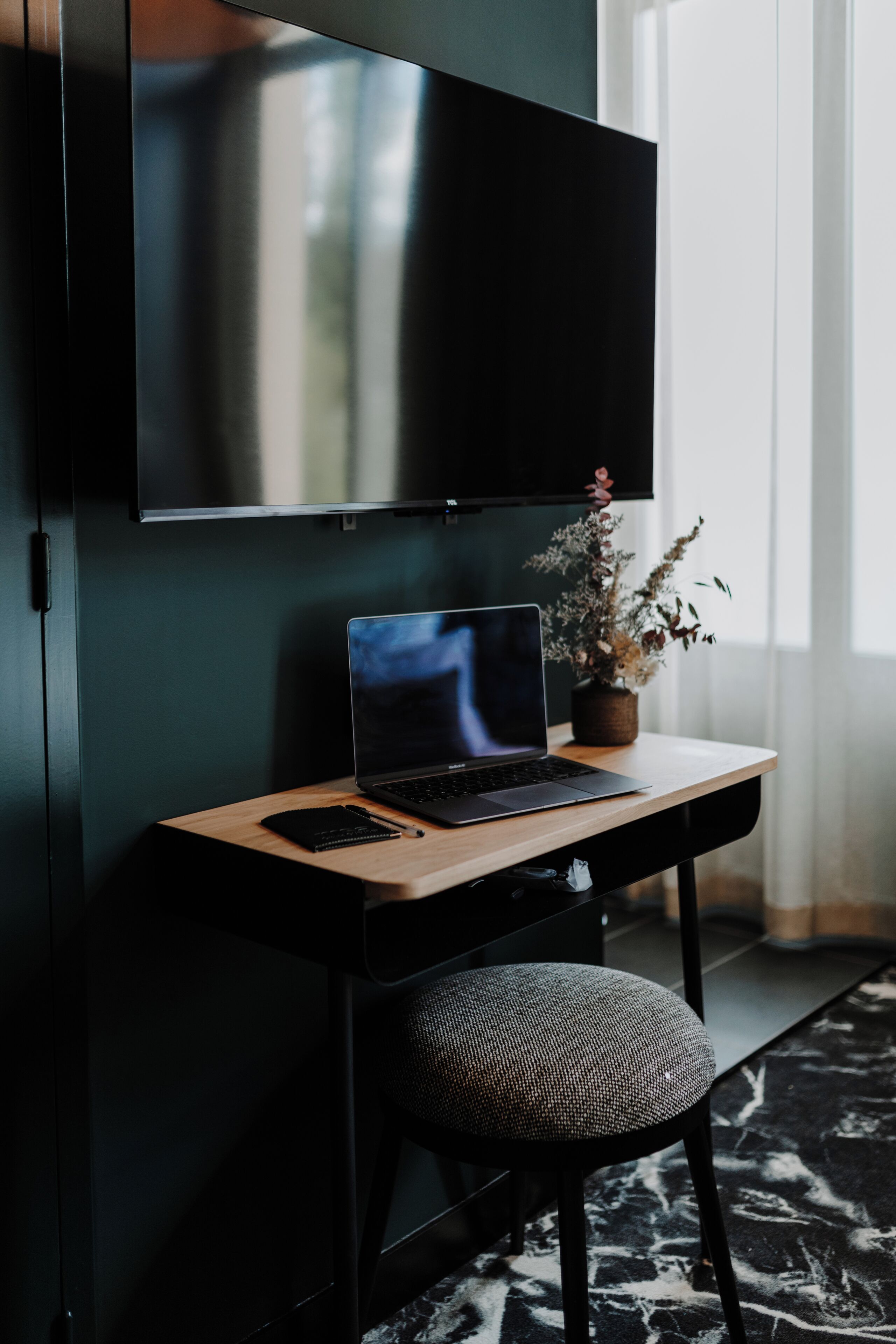 A modern room with a desk, a laptop, a TV, and a potted plant.
