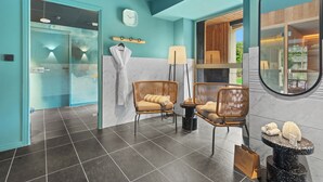 A modern bathroom with a teal color scheme, two wicker chairs, a round mirror, and a small table with toiletries. - Hôtel Le Rituel Honfleur (Honfleur)