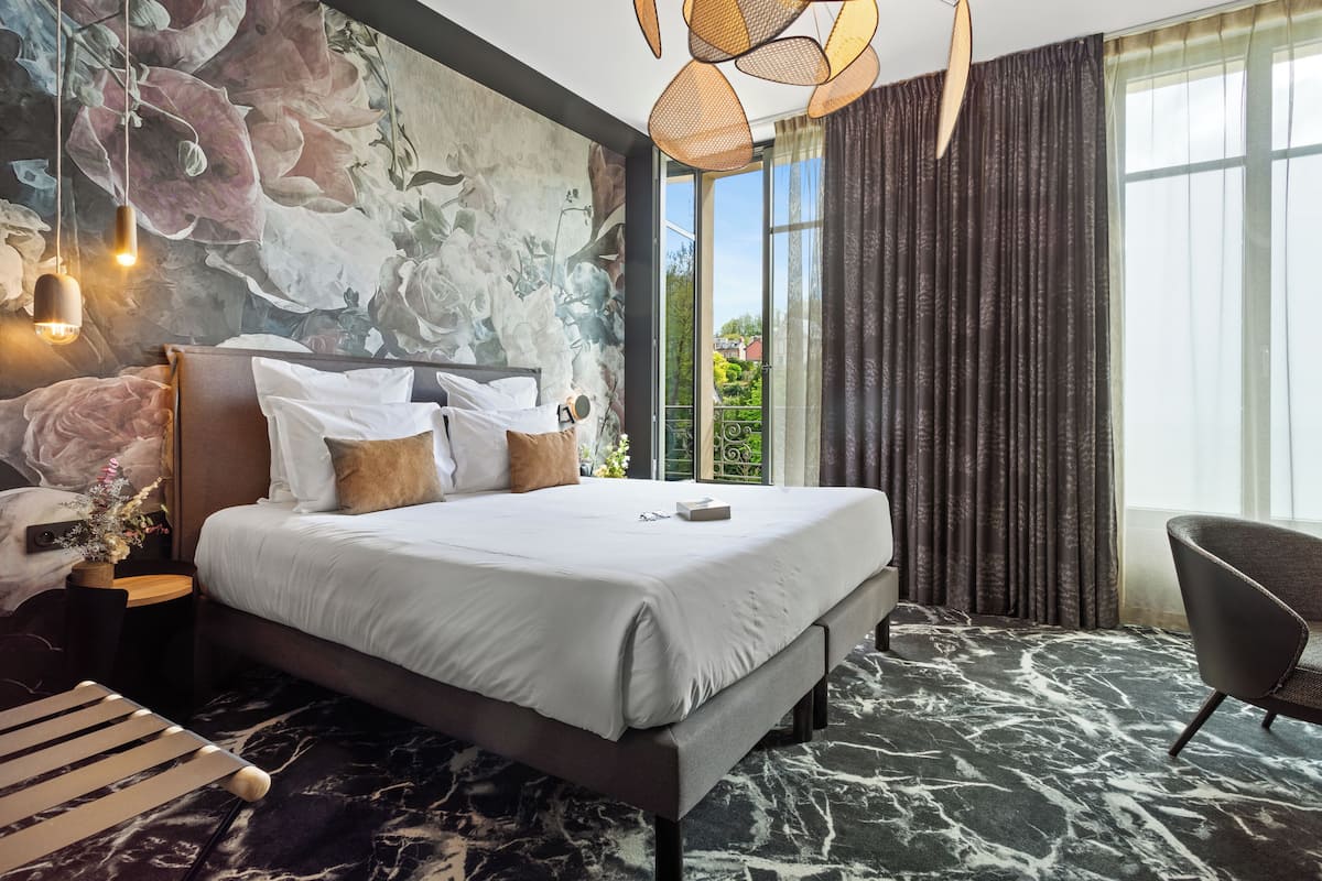 Una habitación de hotel moderna con una cama grande, vistas a zonas verdes por la ventana y un suelo con diseño de mármol.