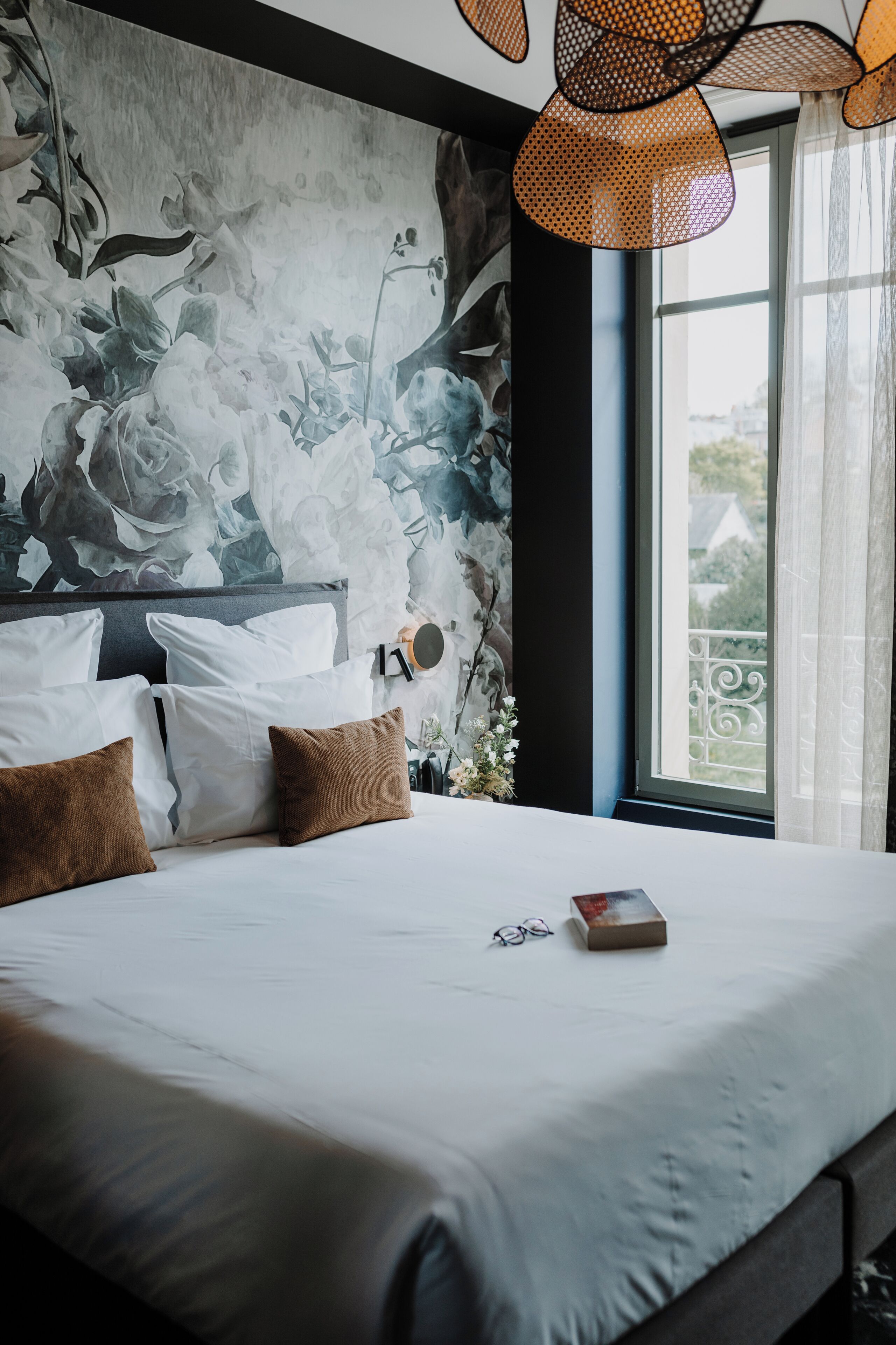 A modern bedroom with a large bed, a wall mural, and a view of the outdoors.