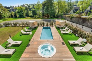 Zona de piscina con un jacuzzi, rodeada de sillones de descanso y una terraza de madera.