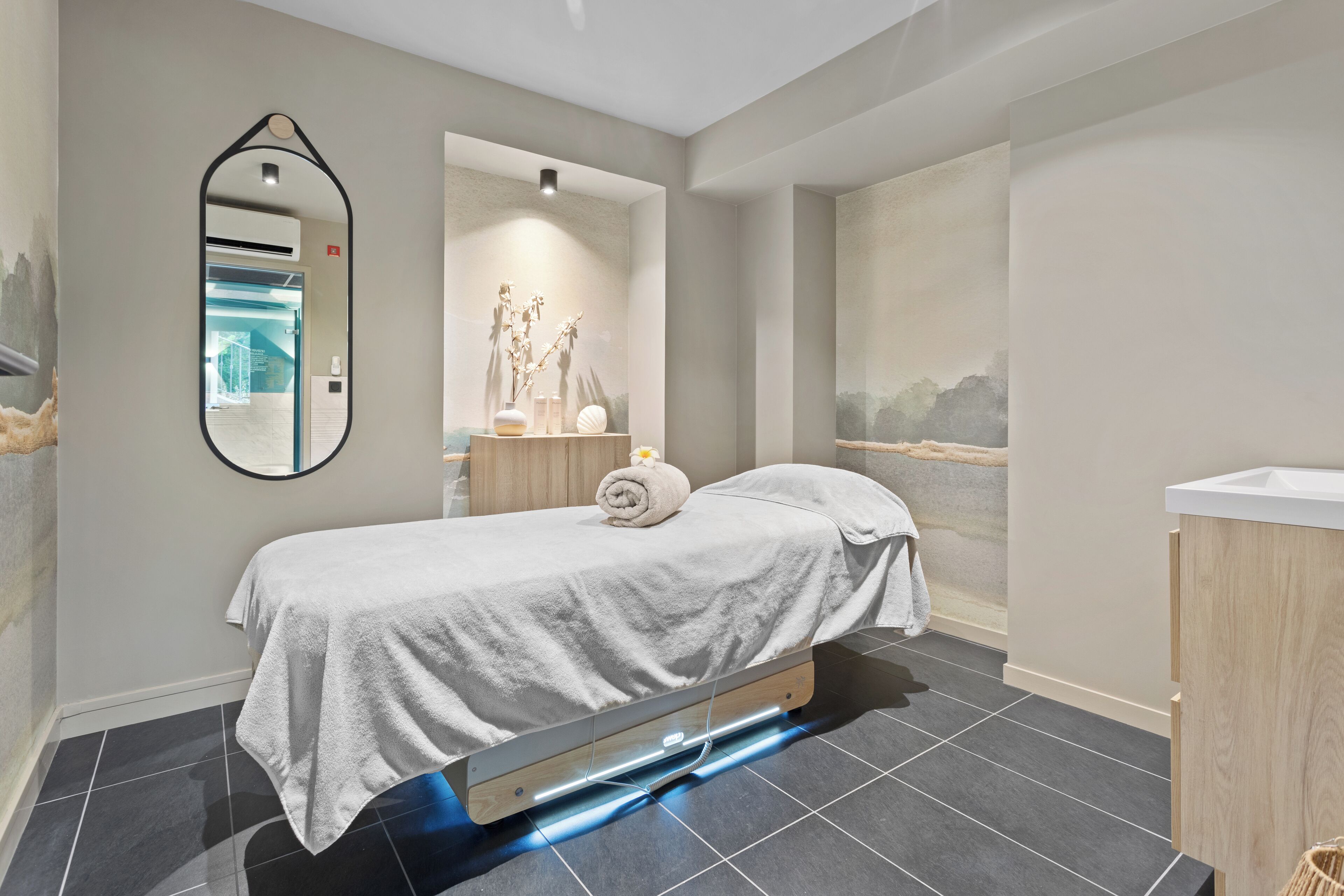 A modern bedroom with a bed, a mirror, a vanity, and a wall-mounted air conditioner.