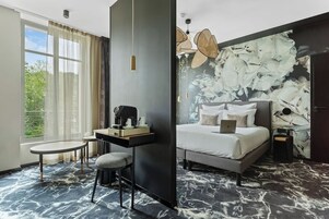 Una habitación de hotel moderna con una cama, un escritorio, una silla y un ventanal con cortinas.