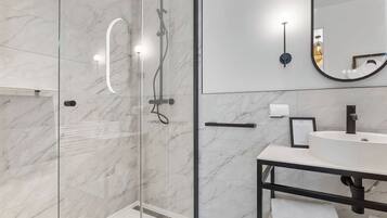A modern bathroom with a glass-enclosed shower, a white sink, and a large mirror.