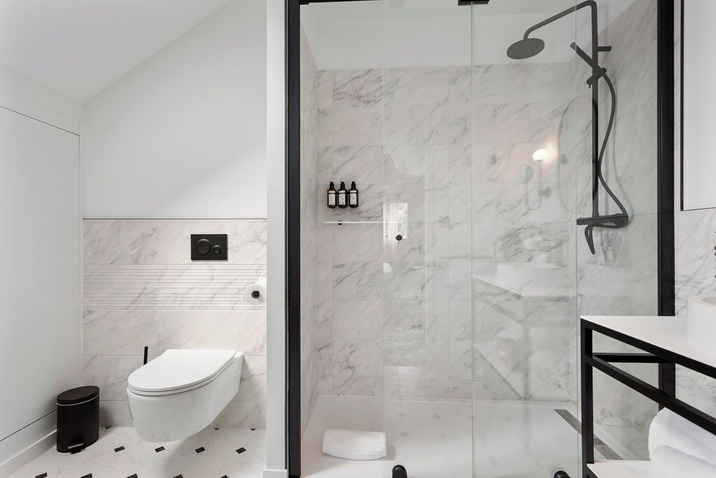 Une salle de bain moderne avec une douche à parois de verre, des toilettes blanches et une poubelle noire.