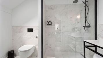 A modern bathroom with a glass-enclosed shower, a white toilet, and a black trash bin.