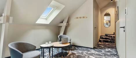 A modern room with a sloped ceiling, a skylight, a marble-patterned floor, a round table with two chairs, and a laptop on the table.