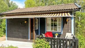 A small wooden cabin with a tiled roof, a porch with a striped awning, and a wooden deck.