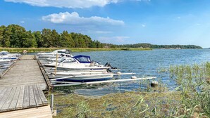 A wooden dock with several boats moored at the end, a clear sky, and a forested shoreline.